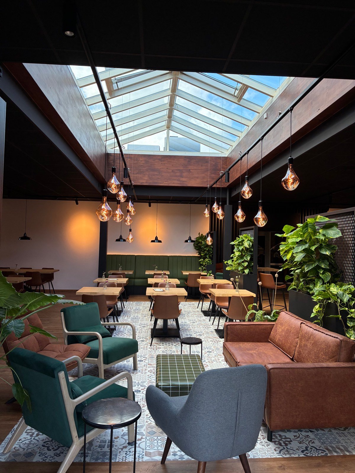 Gemütlicher Loungebereich im Wohnzimmer mit Ledersofas, grünen Sesseln, Pflanzen und großem Oberlicht